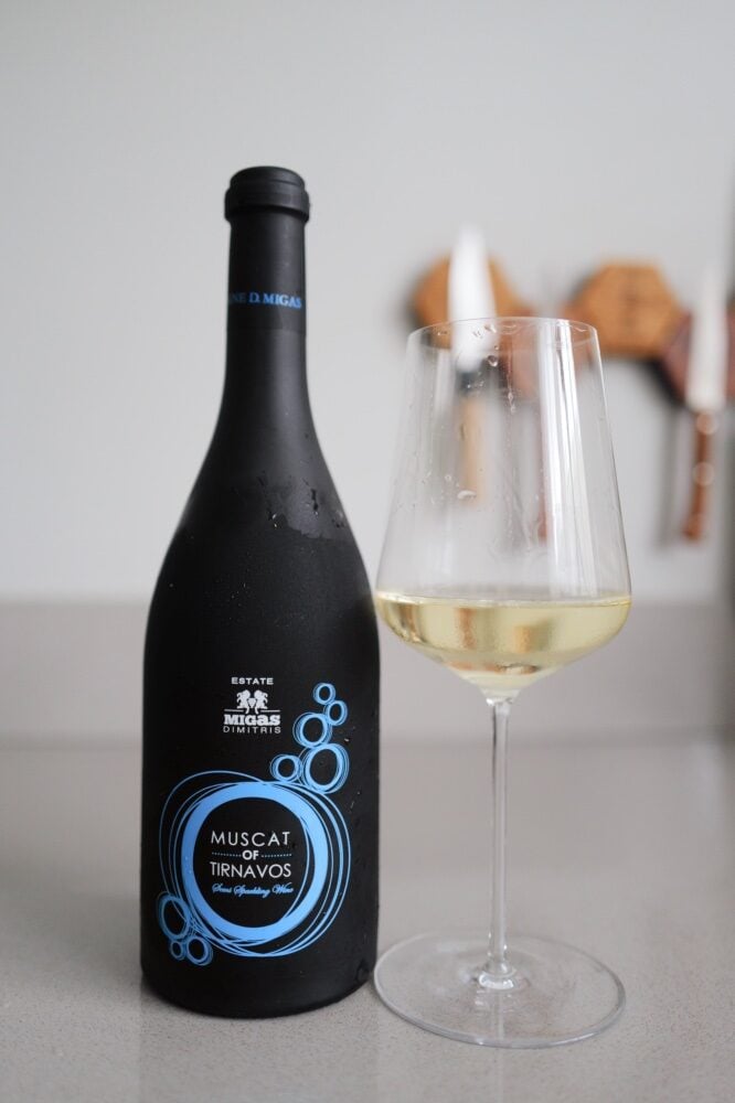 Fles Domaine Migas Muscat of Tirnavos mousserend naast glas witte wijn