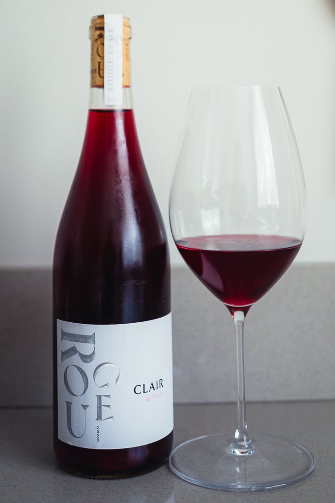 Fles Rouge Clair 2023 met een glas rode wijn ernaast