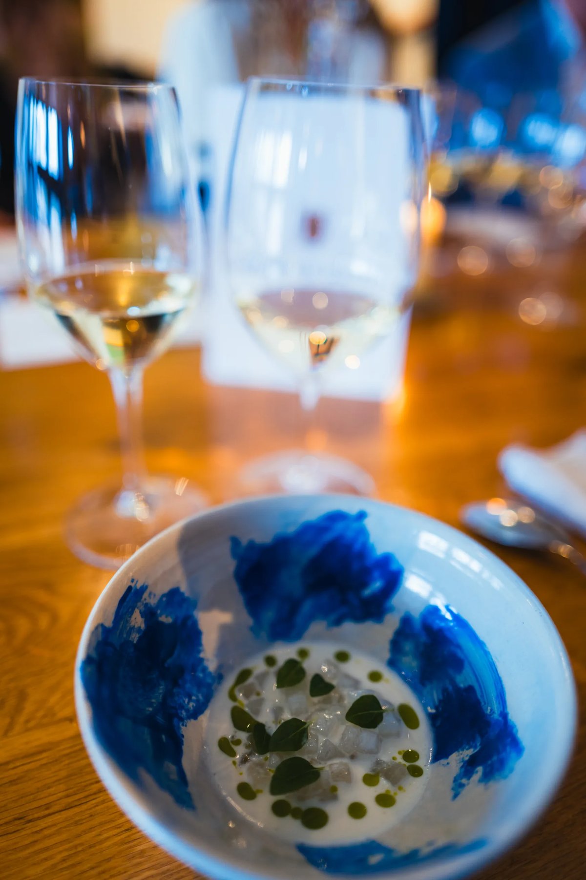 Blauw-wit schaaltje met gerecht en twee glazen witte wijn op een houten tafel