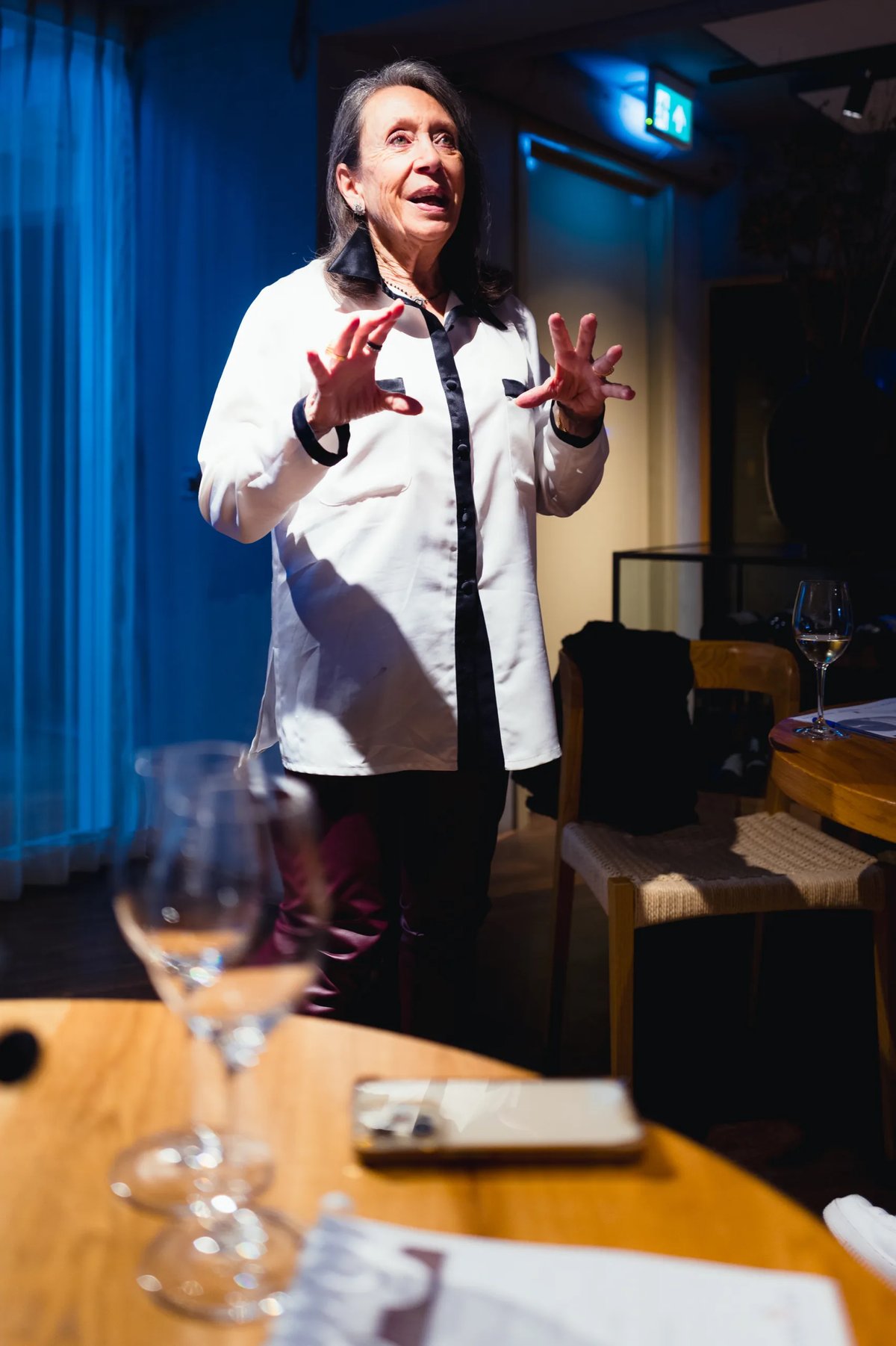 Vrouw in witte blouse staat te vertellen met geheven handen in het restaurant