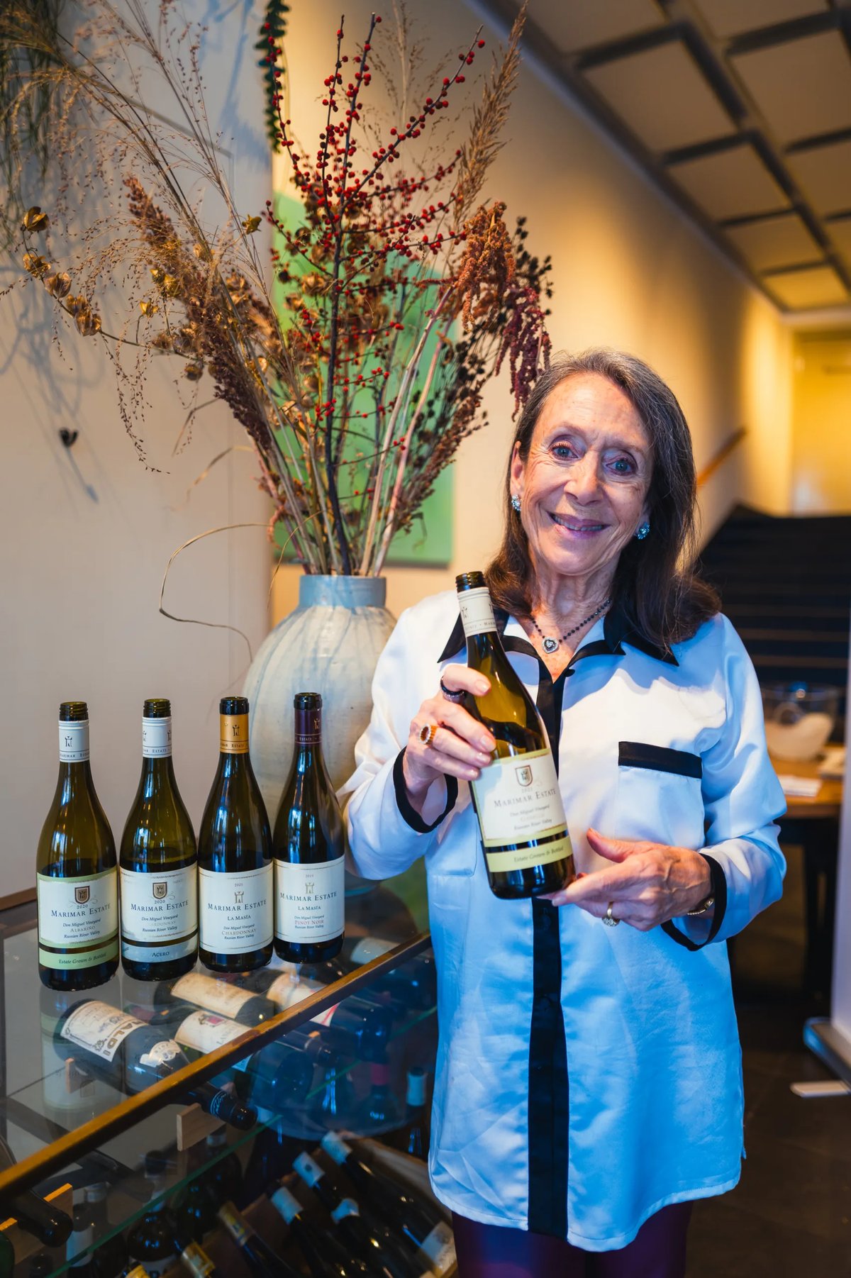 Vrouw in lichtblauwe blouse presenteert een fles Marimar Estate witte wijn