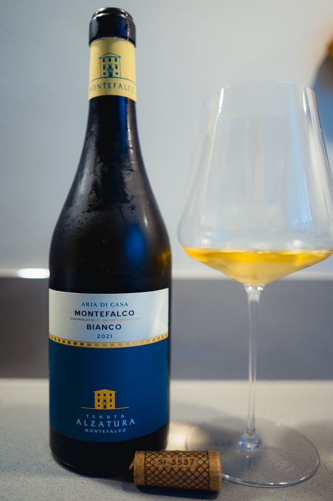 Fles Aria di Casa Montefalco Bianco 2021 met een glas goudkleurige witte wijn en kurk