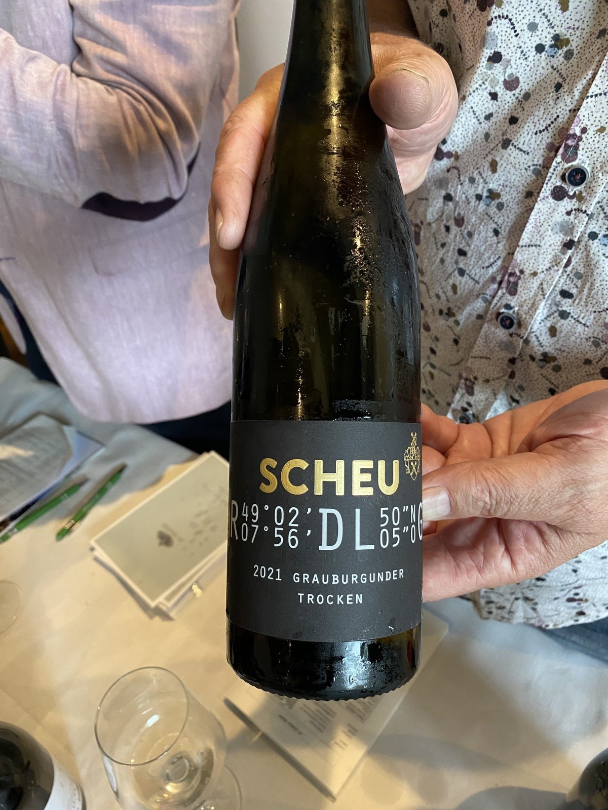 Handen houden een fles Scheu DL Grauburgunder Trocken met zwart etiket vast