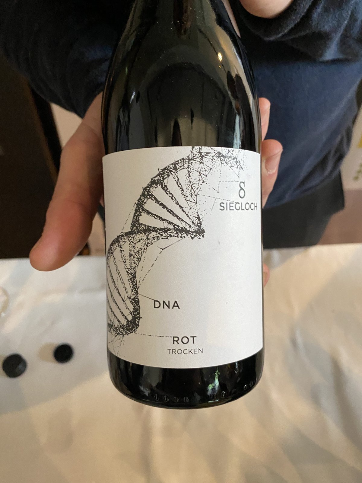 Hand houdt een fles Siegloch DNA Rot Trocken met DNA-helix op het etiket