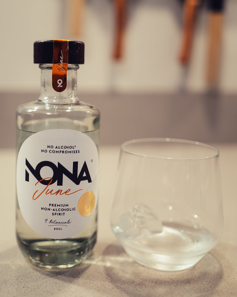 Fles NONA Ginger, gouden alcoholvrije spirit, op tafel met onscherpe achtergrond