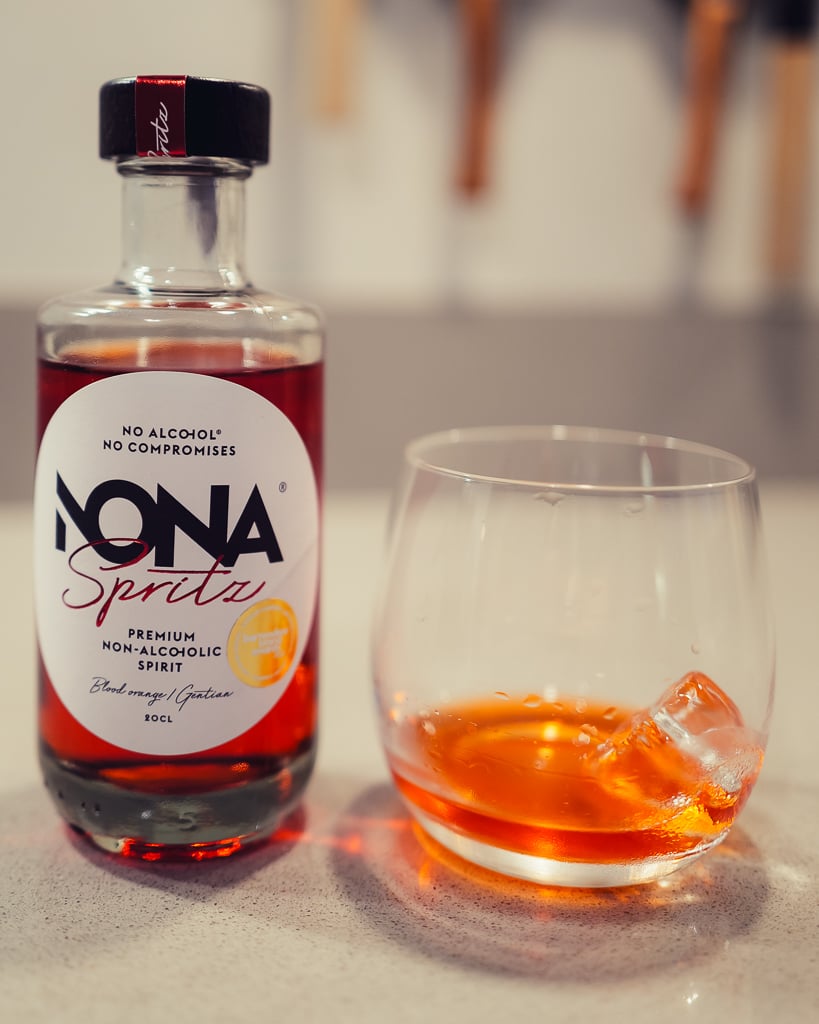 Fles NONA June met glas heldere drank op ijs op een lichte tafel