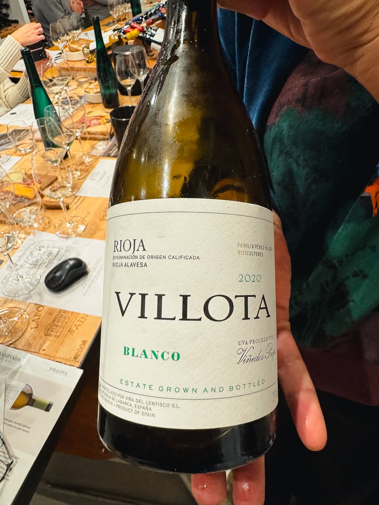 Carmen Pérez houdt een fles Villota Blanco vast aan een gedekte proeftafel