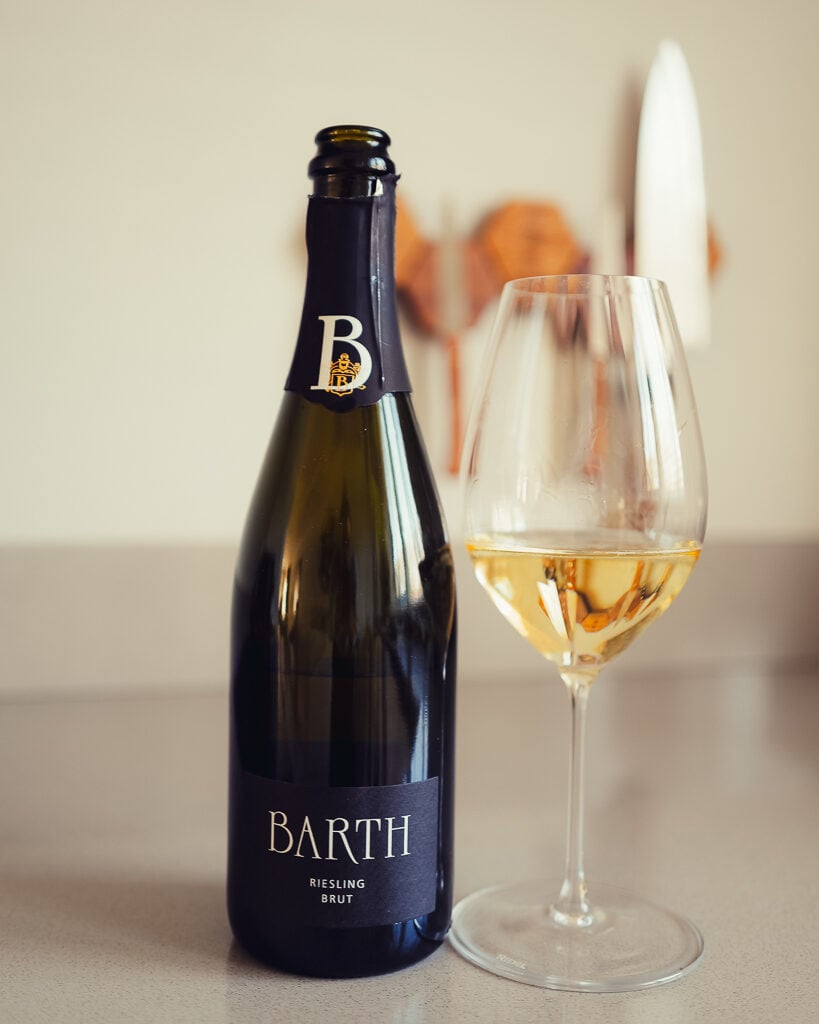 Fles Barth Riesling Brut uit de Rheingau naast een glas goudgele mousserende wijn