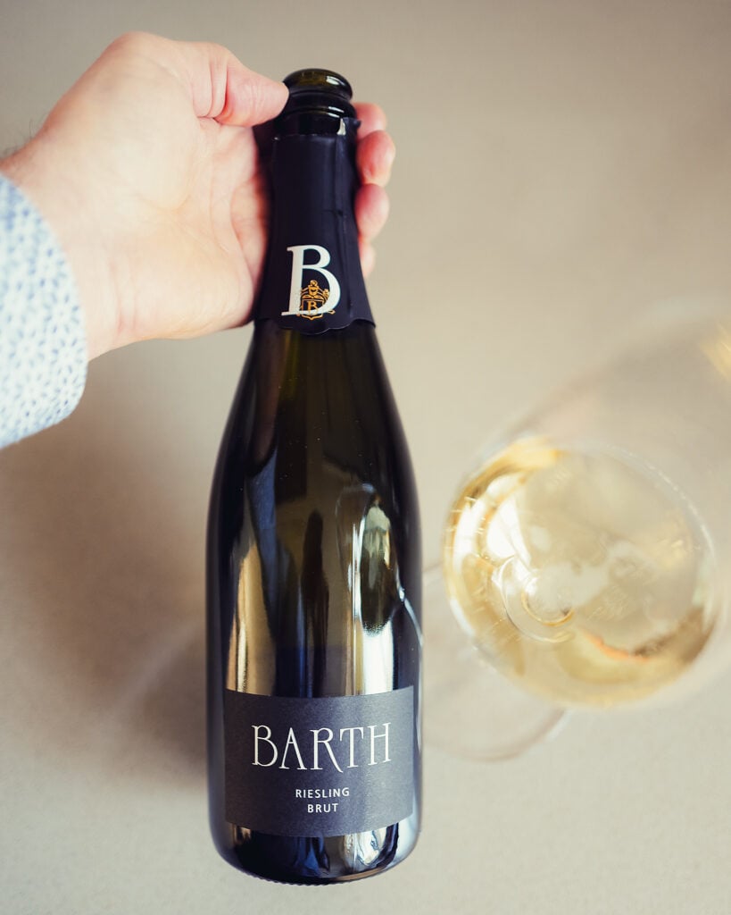 Hand houdt fles Barth Riesling Brut boven een glas mousserende wijn