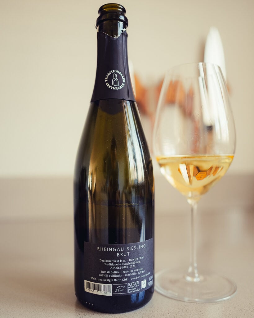 Achterkant van een fles Barth Rheingau Riesling Brut naast een glas mousserende wijn