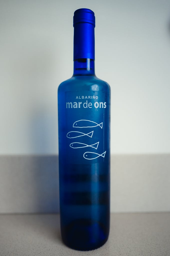 Diepblauwe fles Mar de Ons Albariño met visjes-illustratie op een lichte achtergrond