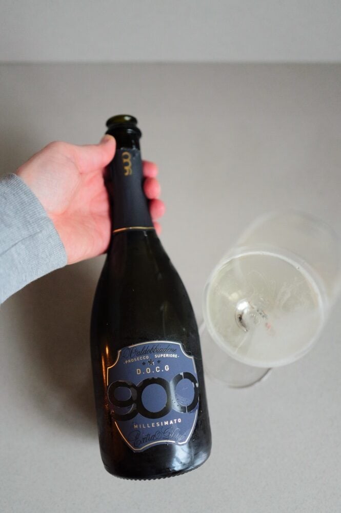 Fles 900wine DOCG Valdobbiadene Prosecco met blauw etiket naast een glas mousserende wijn