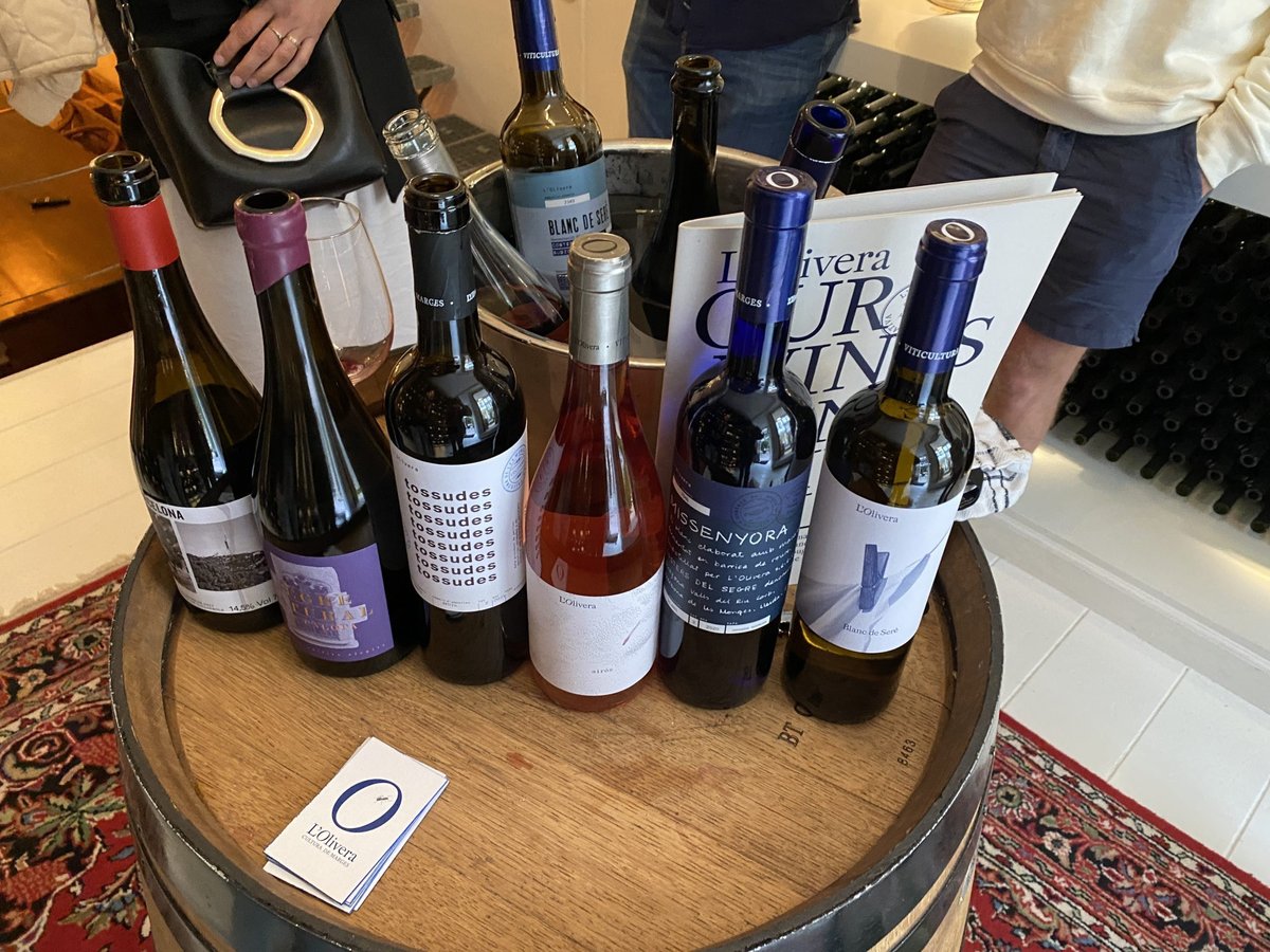 Acht flessen van L'Olivera en Can Calopa, wit, rosé en rood, op een wijnvat met brochure