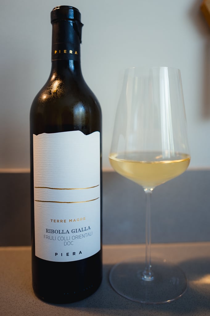 Fles Piera Ribolla Gialla naast een glas lichtgele wijn op een aanrecht