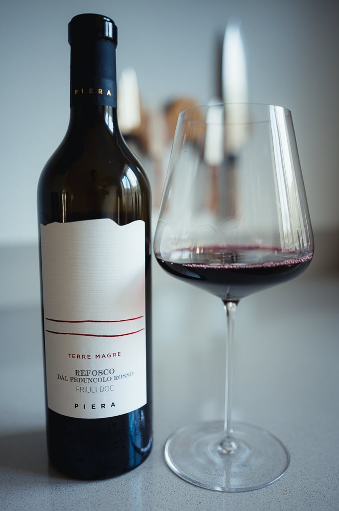 Fles Piera Refosco dal Peduncolo Rosso naast een glas dieprode wijn op een aanrecht