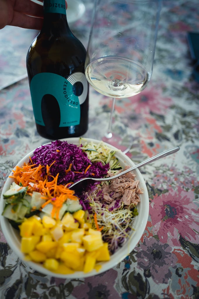 Fles Piera ZeroDiZero White met een glas wijn naast een kleurrijke salade op een gebloemd tafelkleed
