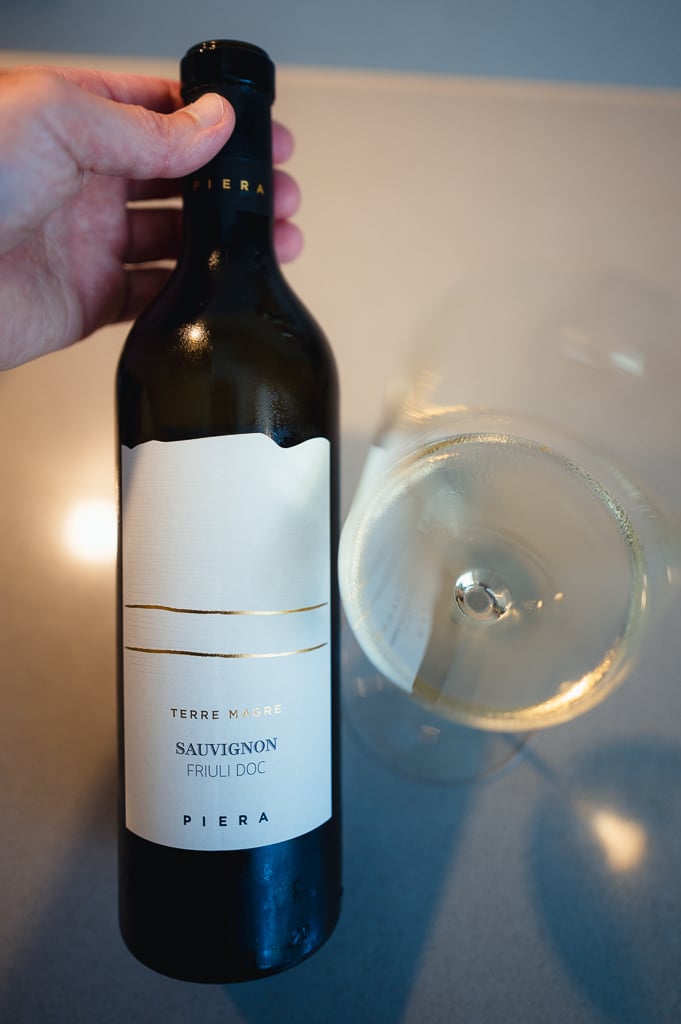 Hand houdt fles Piera Sauvignon uit Friuli naast een glas lichtgele wijn