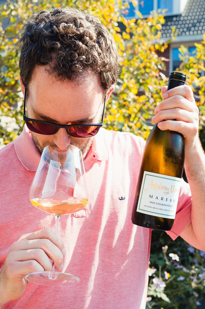 Man met zonnebril ruikt aan glas witte wijn met fles Arterberry Maresh Maresh in de hand