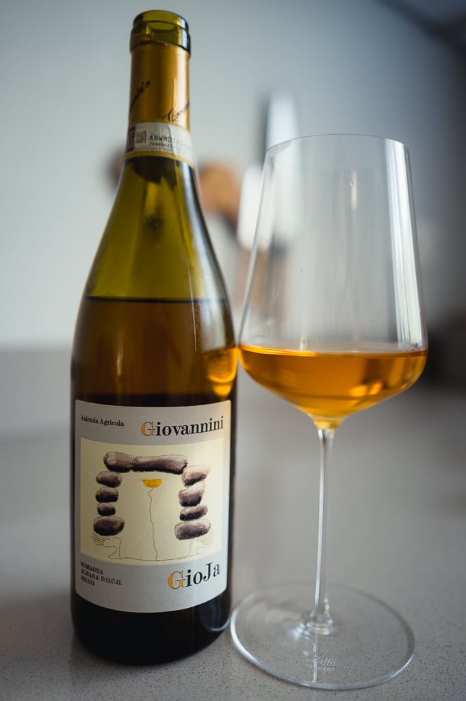 Fles Giovannini GioJa Albana DOCG en glas oranje witte wijn met onscherpe achtergrond