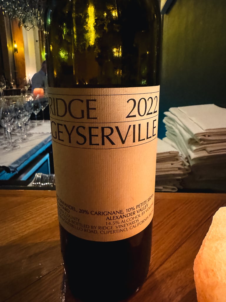 Achterkant van fles Ridge Geyserville 2022 met beschrijvende tekst in een wijnbar