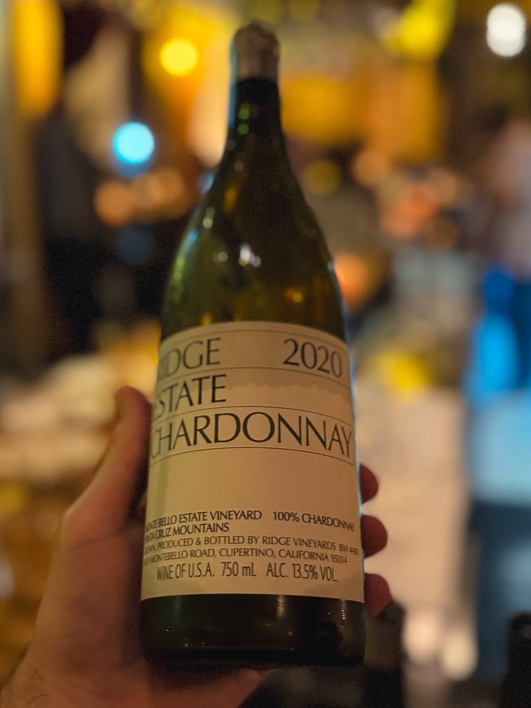 Hand houdt fles Ridge Monte Bello 2021 vast in een schemerige wijnbar