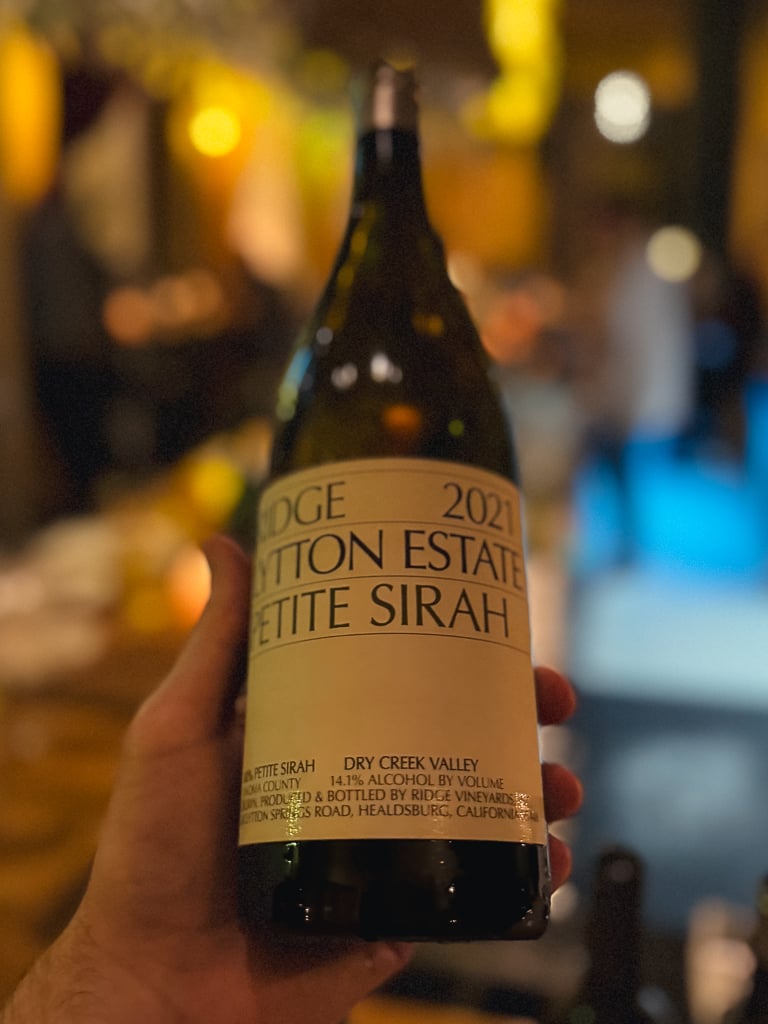 Hand houdt fles Ridge Estate Chardonnay 2020 vast in een warm verlichte bar
