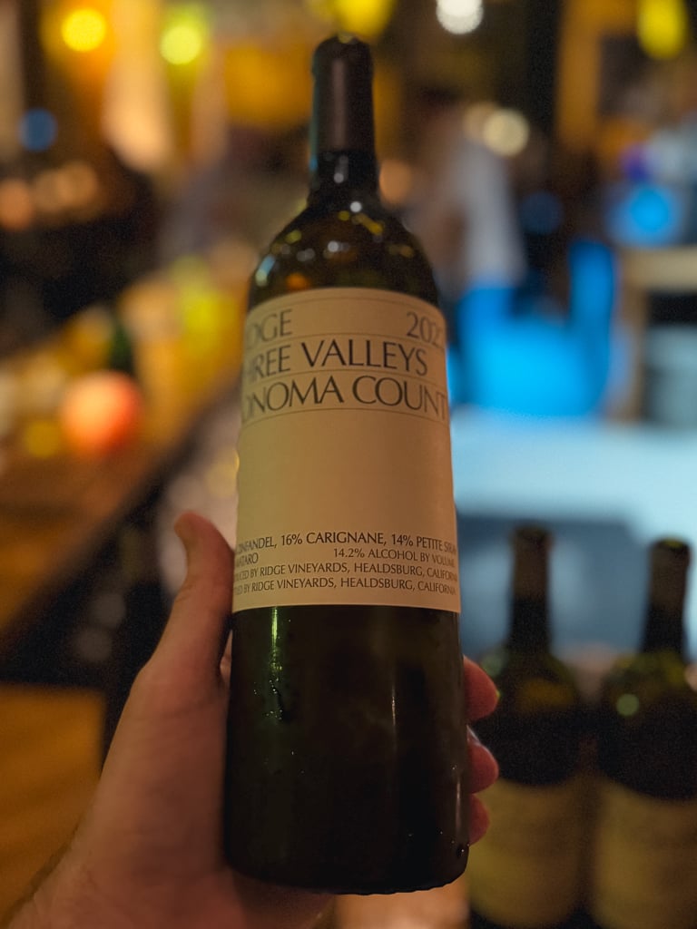 Hand houdt fles Ridge Lytton Estate Petite Sirah 2021 vast in een wijnbar