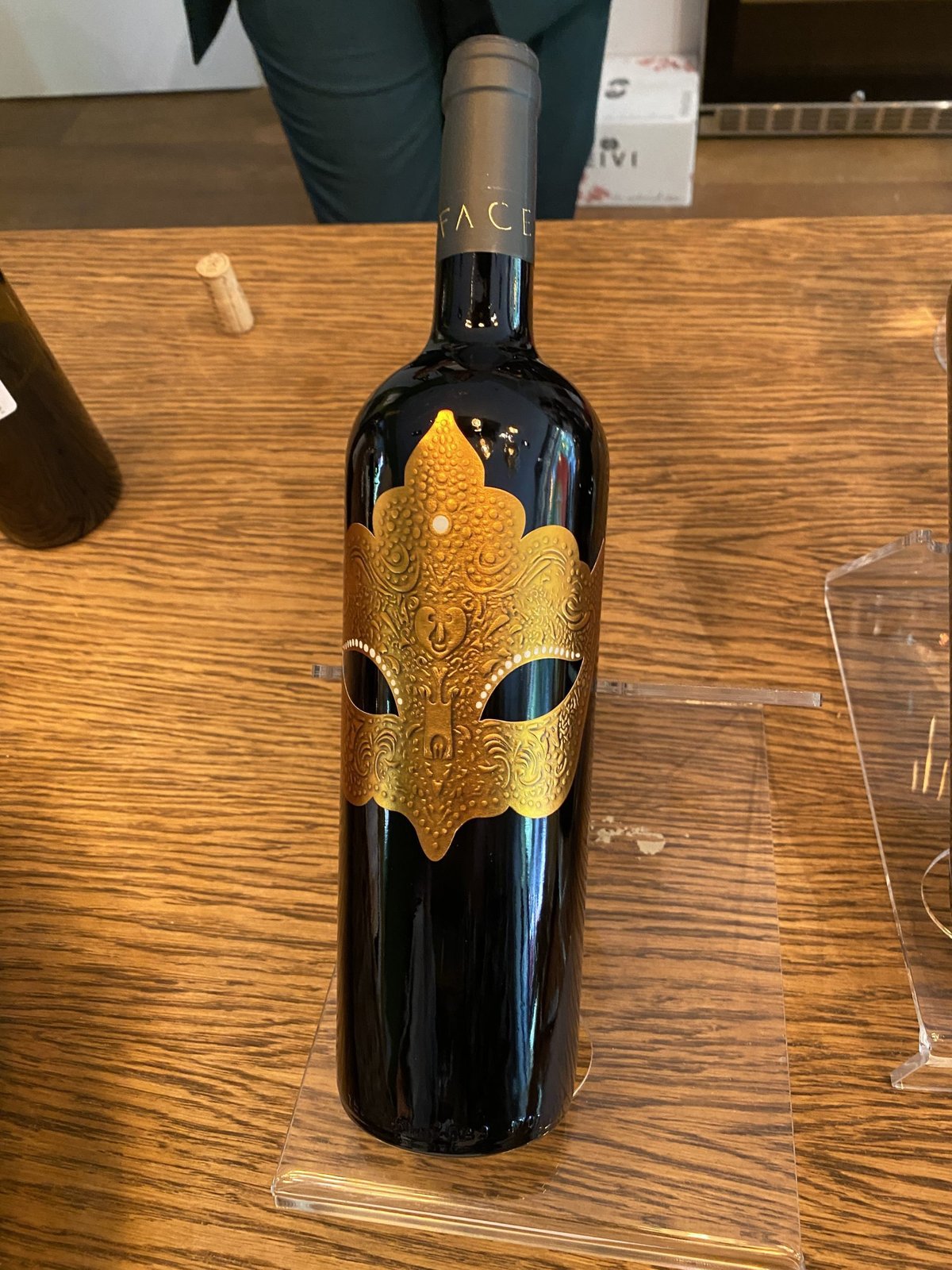 Fles Volte-Face rode wijn met een gouden masker op het etiket op een standaard