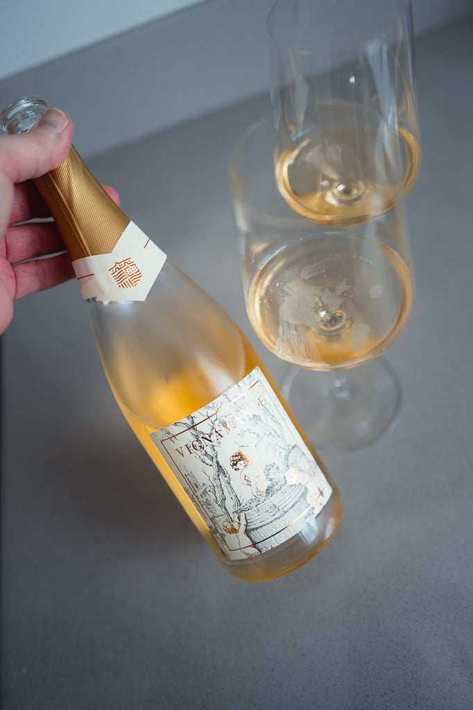 Hand kantelt fles Vignamante rosé naast twee glazen mousserende wijn van bovenaf