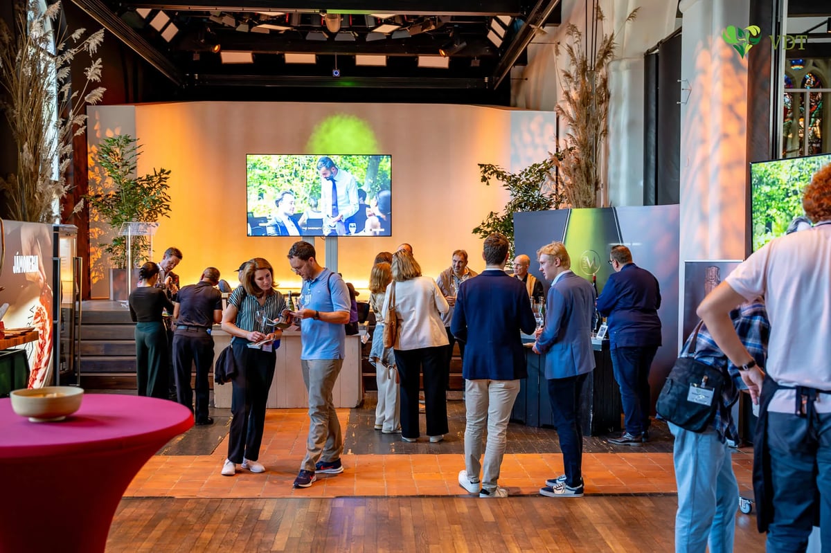 Bezoekers rond statafels bij een champagne-evenement met groot videoscherm