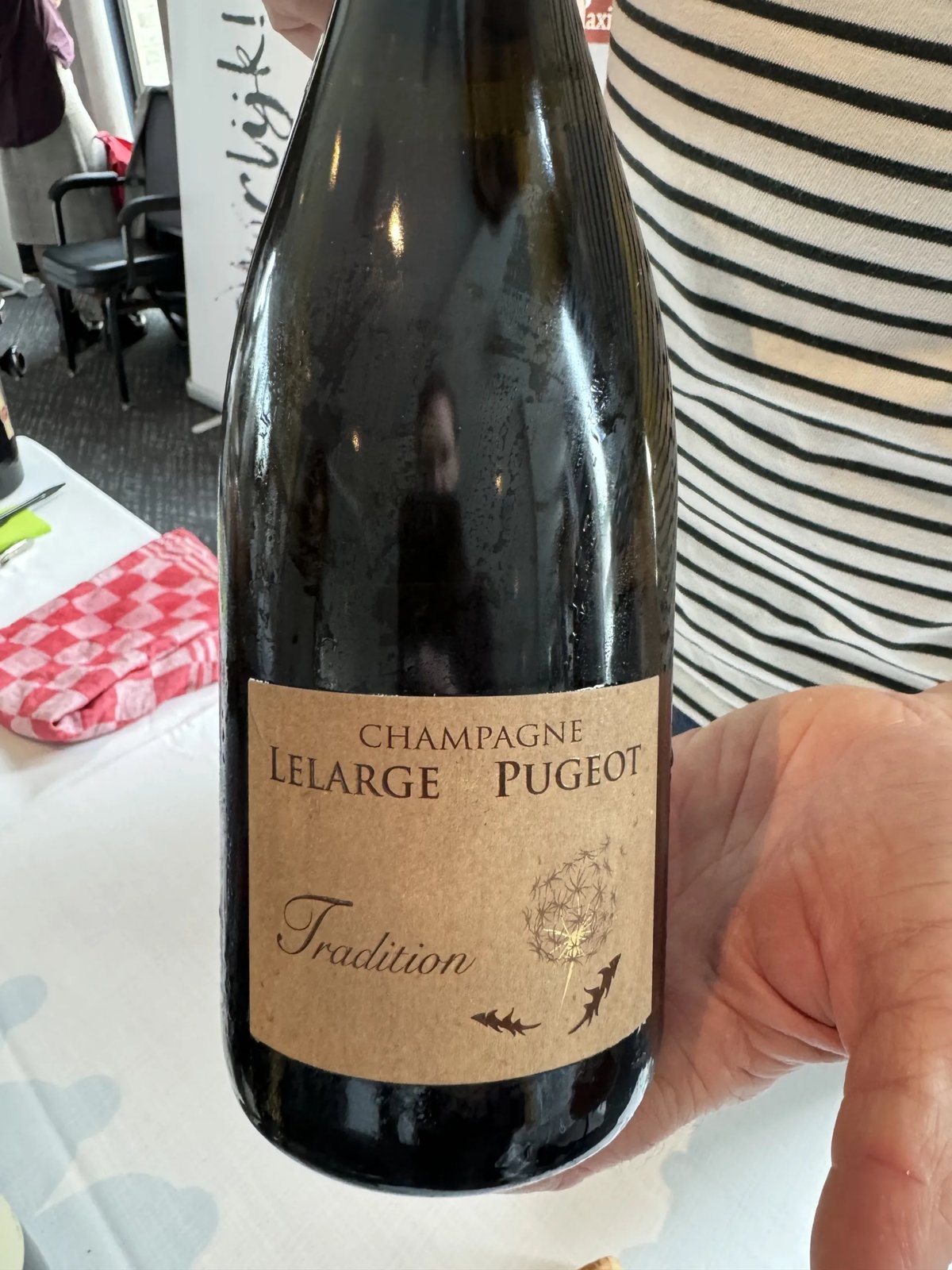 Fles Champagne Lelarge-Pugeot Tradition met kraftpapier-etiket in een hand