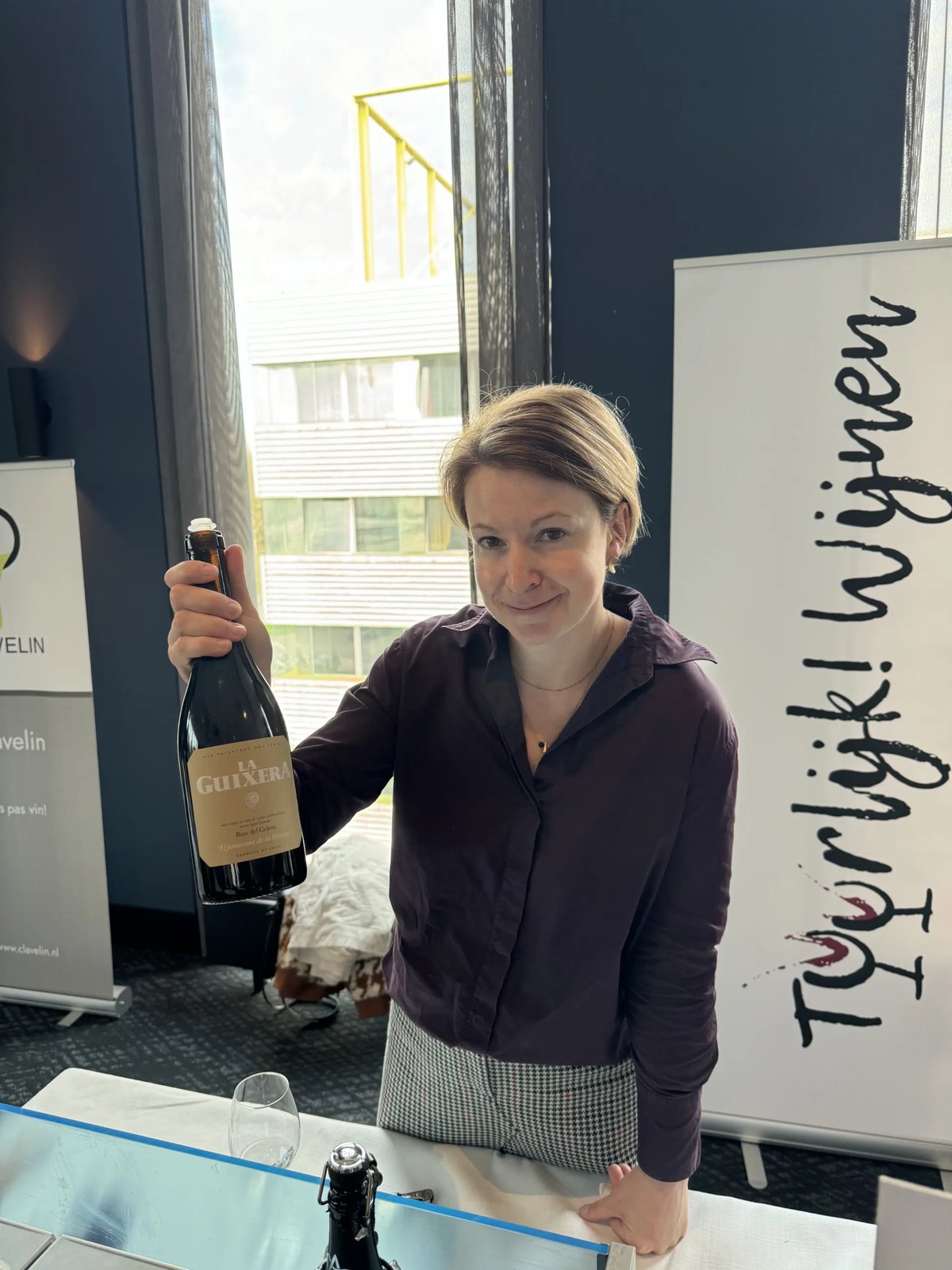 Vrouw bij stand TuurlijkWijnen toont een fles rode wijn aan de proeftafel