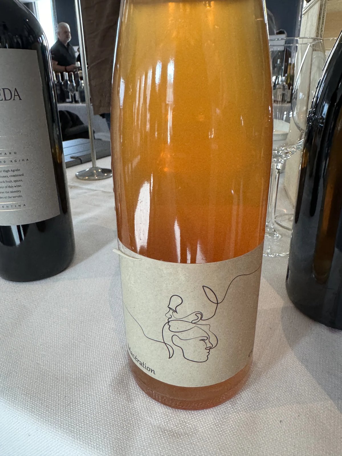 Fles oranje wijn met een lijntekening van een gezicht op het etiket op een proeftafel