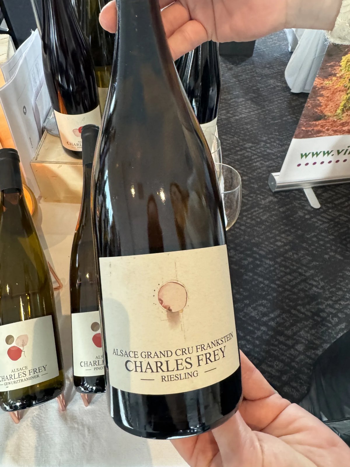 Hand houdt fles Charles Frey Riesling Grand Cru Frankstein vast bij een proefstand