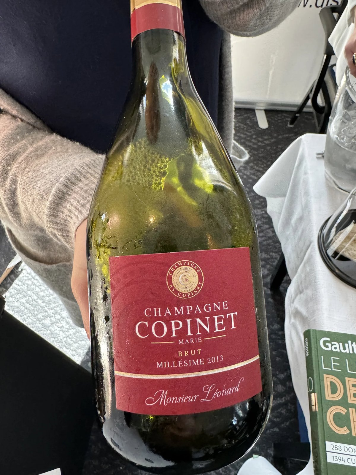 Fles Champagne Marie Copinet met rood etiket vastgehouden boven een proeftafel