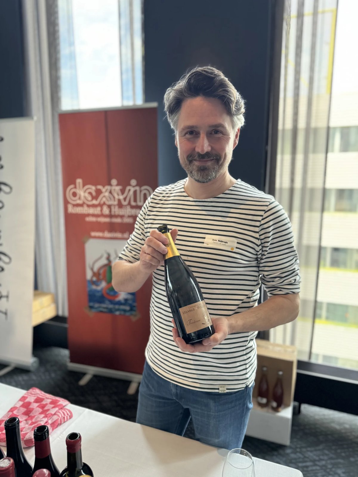 Man in gestreept shirt toont een fles champagne aan een proefstand bij Daxivin