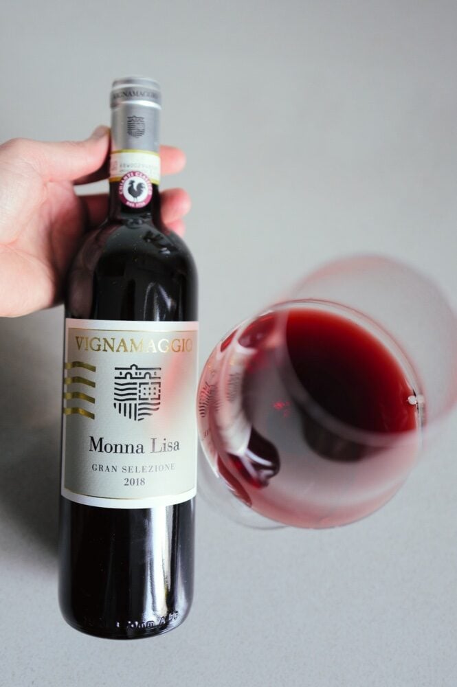 Hand kantelt fles Vignamaggio Monna Lisa naast een liggend glas rode wijn van bovenaf