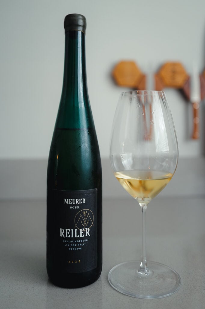 Donkergroene fles Meurer Reiler Riesling naast een glas witte wijn op een aanrecht