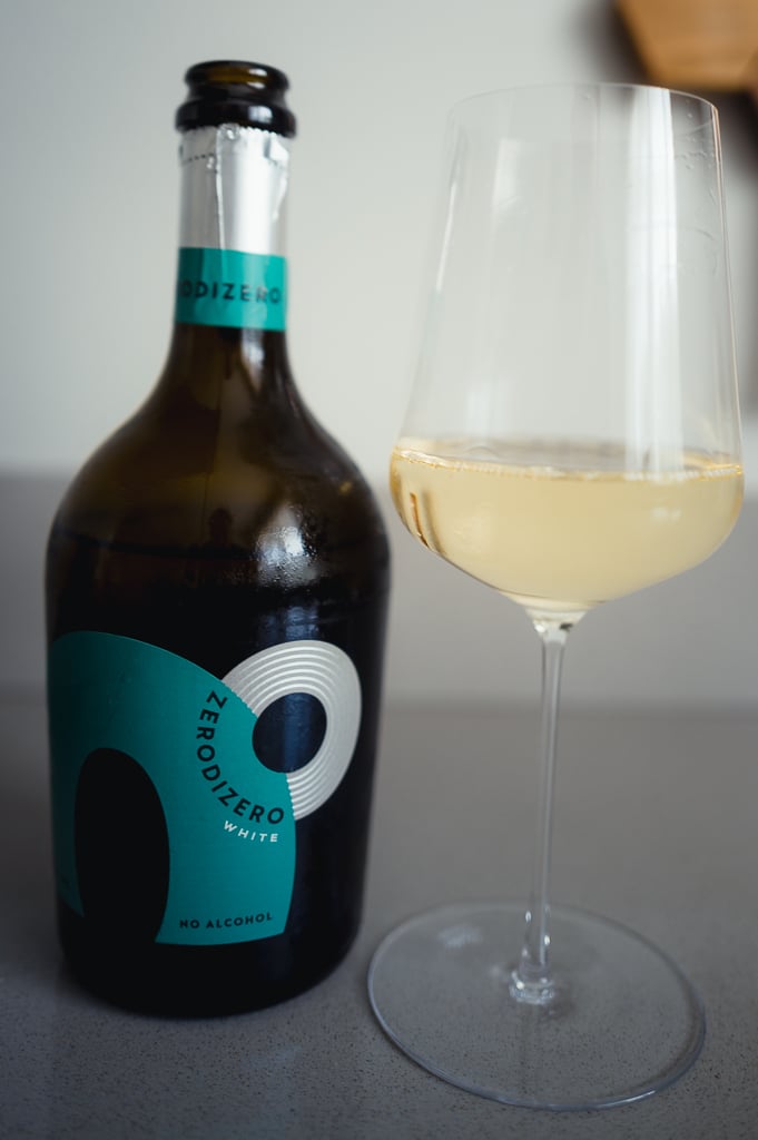 Fles Zero di Zero White met tealblauw etiket naast een gevuld glas lichte mousserende drank