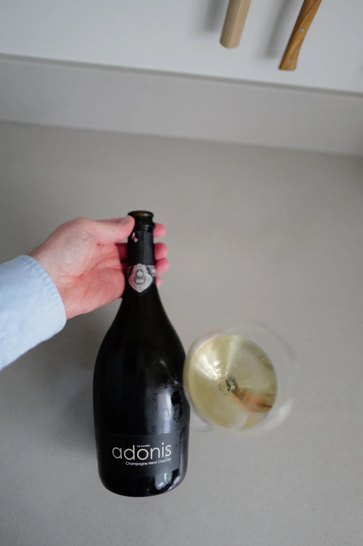 Fles Henri Chauvet Adonis 2020 met het front-label, naast een glas champagne