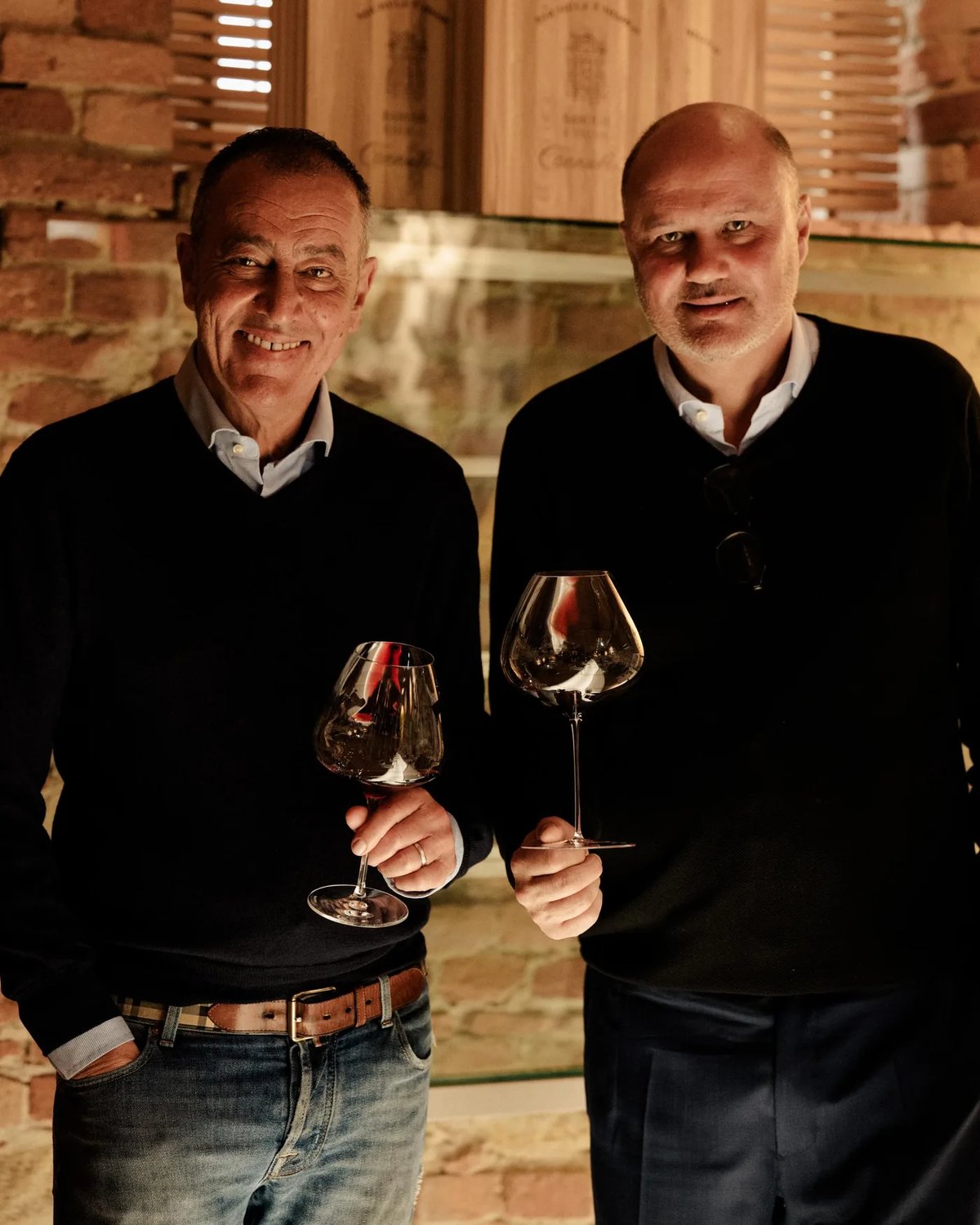 Alberto en Stefano Chiarlo met een glas rode wijn voor een bakstenen muur