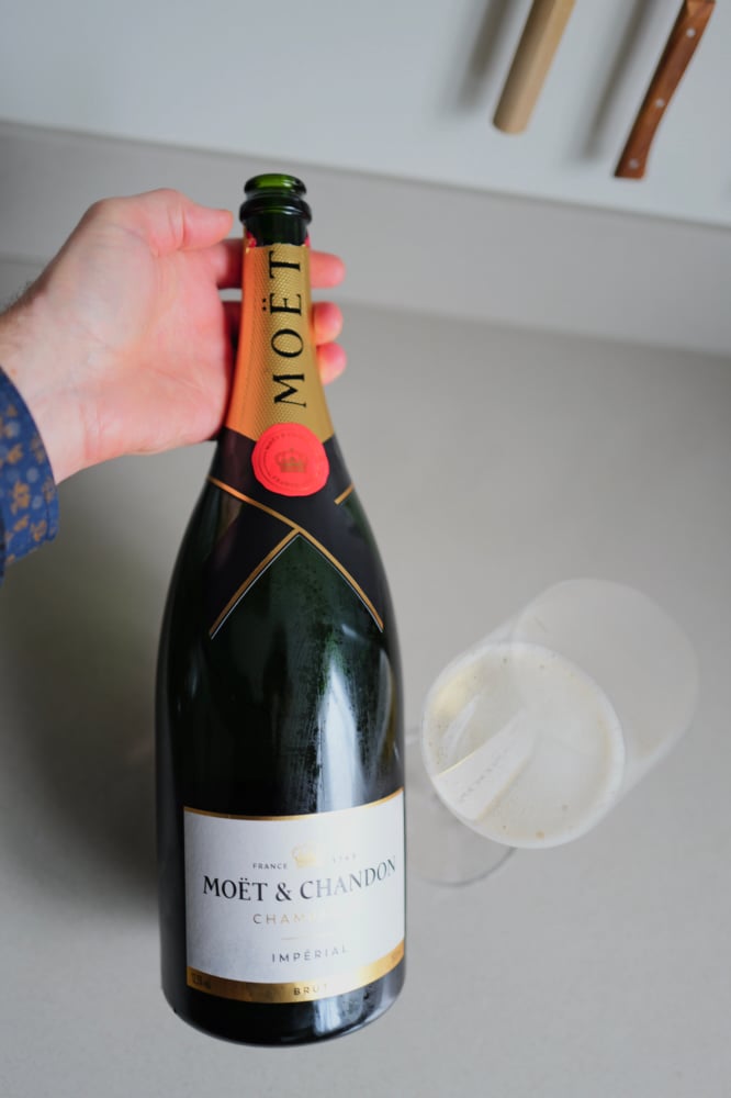 Hand holding the Moët & Chandon Brut Impérial magnum next to two glasses on a counter