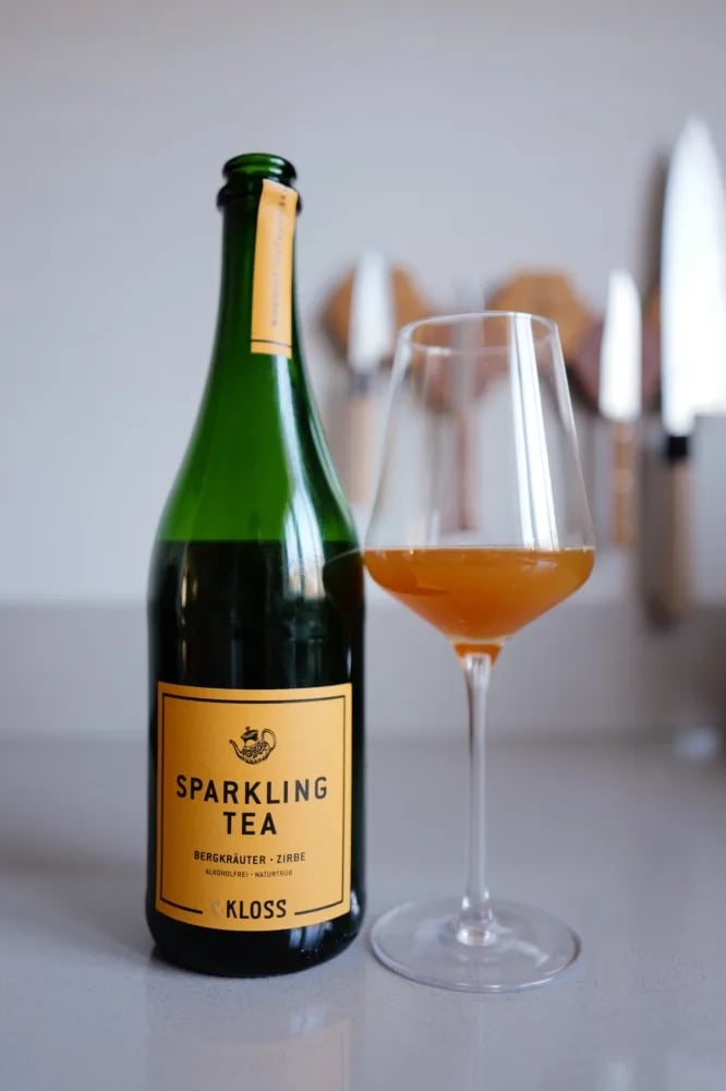 Fles Sparkling Tea Bergkraeuter van C. Kloss met geel etiket, naast een glas oranje thee