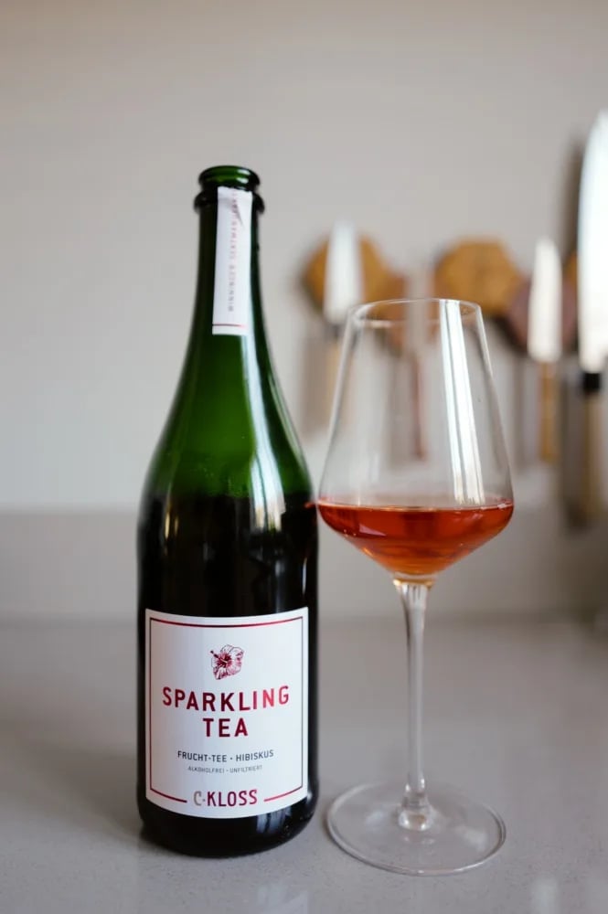 Fles Sparkling Tea Fruit Tea van C. Kloss met wit-rood etiket, naast een glas roodoranje thee