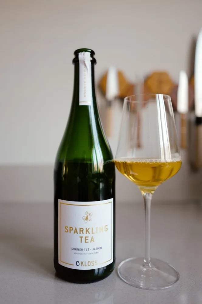 Fles Sparkling Tea Green Tea van C. Kloss met wit etiket, naast een glas goudgele thee