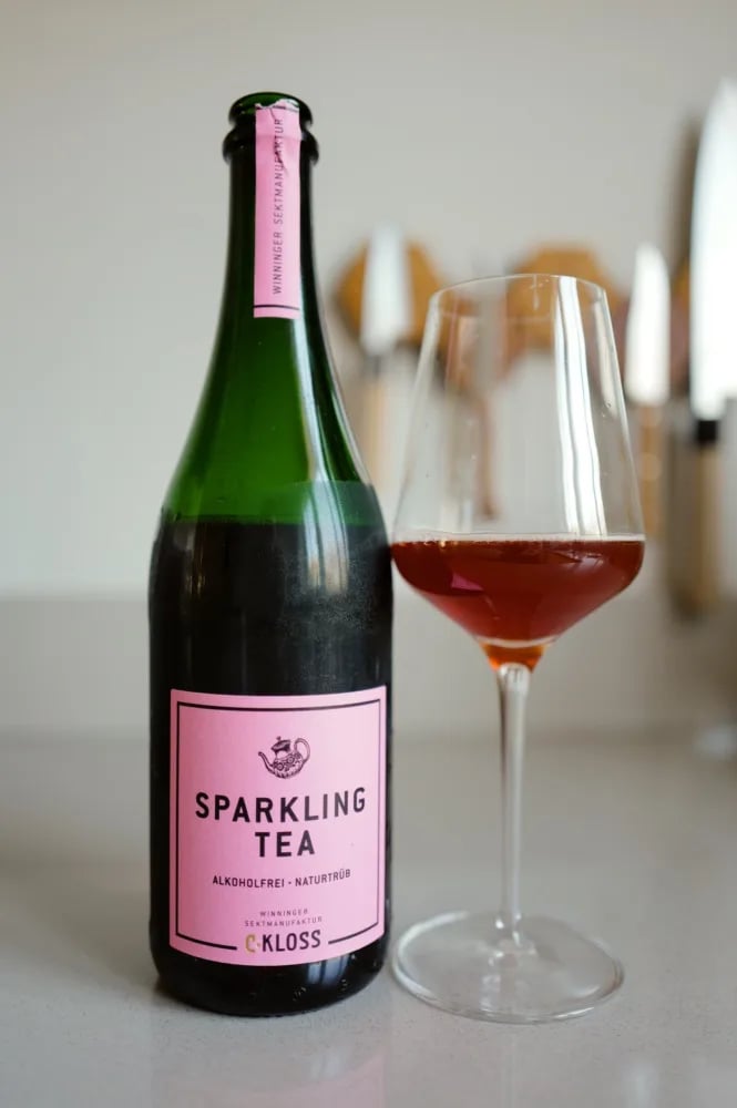 Fles Sparkling Tea Rose van C. Kloss met roze etiket, naast een glas rode thee