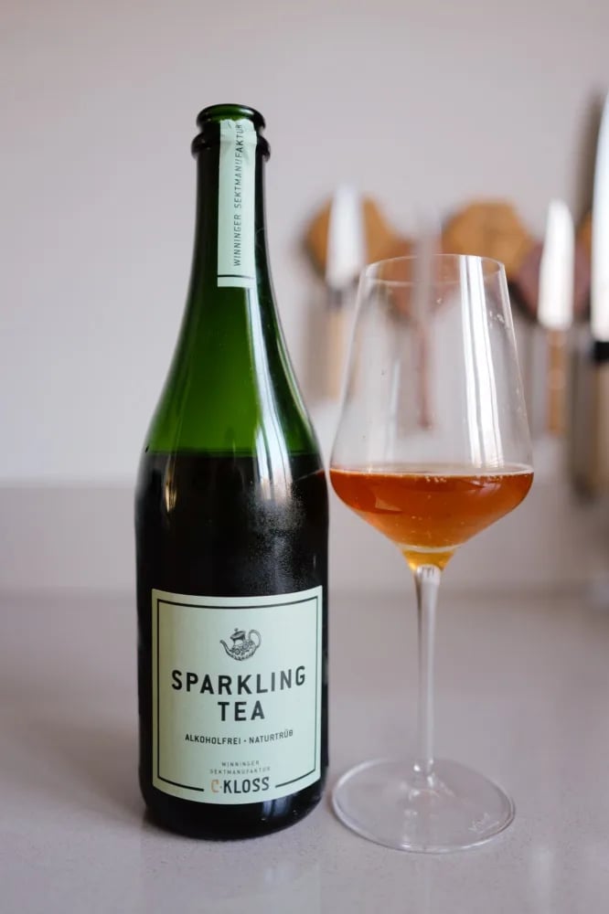 Fles Sparkling Tea Weiss van C. Kloss met mintgroen etiket, naast een glas amberkleurige thee