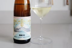 Fles Kolonne Null Gelblack alcoholvrije Riesling naast een glas witte wijn op een licht keukenblad