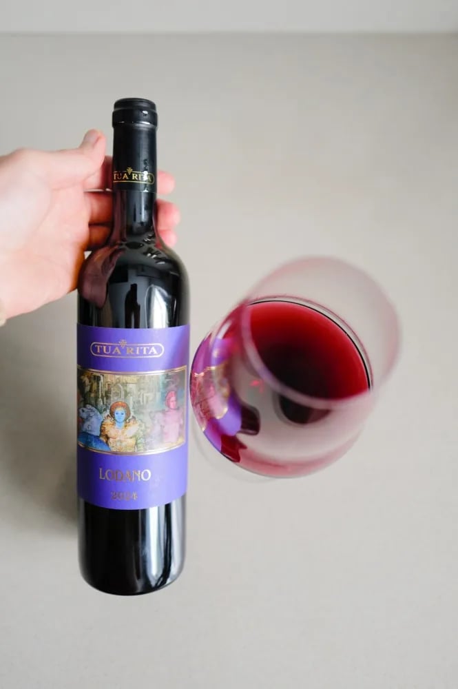 A glass of Lodano Rosso 2024 tilted beside the bottle, deep ruby