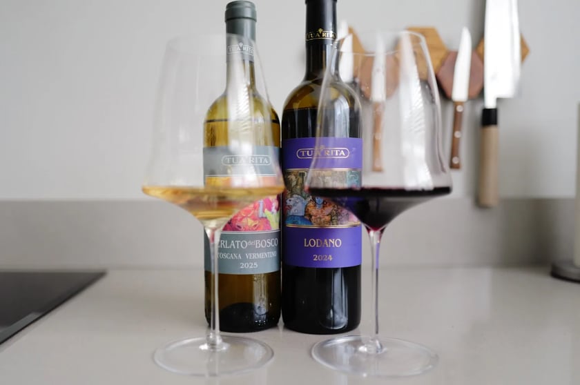 Fles Perlato del Bosco Vermentino 2025 en fles Lodano 2024 van Tua Rita naast elkaar op het aanrecht, met een glas witte en een glas rode wijn